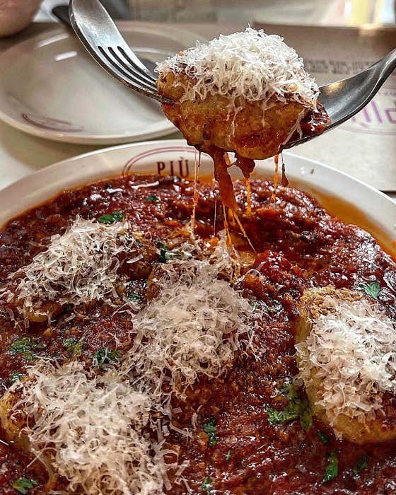 Gnocchi lifted with a fork from cheese-topped sauce
