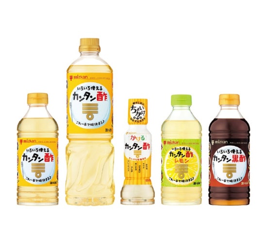 お酢で血糖値をコントロールする健康的な食生活 お酢を使った健康的な食事風景。色とりどりのサラダにお酢をかけている様子、50代女性が台所で料理をしている明るいイメージ