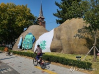 위드코로나 원시인조형물에 여행배낭 설치