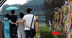 희마의 메시지 메달린 철책 옆 걷는 관광객들