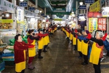 노란 앞치마에 빨간 고무장갑 끼고 시장에서 춤추는 사람들