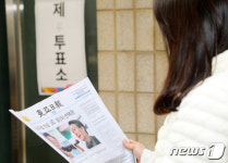 투표소 앞에서 신문 읽는 유권자