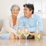 Front view of a mature couple sitting on sofa relaxing with bottle of wine and two glasses in front of them 이미지 (skd230058sdc)... 