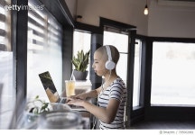 705002861 | 게티이미지코리아 | Teenage girl with shaved head with headphones using laptop at cafe window Royalty-Free 이미지