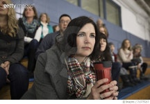 713775217 | 게티이미지코리아 | Serious mother drinking coffee watching ice hockey game in stadium bleachers Royalty-Free 이미지