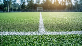 Close-up view of pristine artificial grass on a soccer field with a clear white line marking the playing area under natural... 