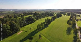Aerial shot of an idyllic, sunlit golf course in the middle of the countryside with trees, vines and fields in the background Stock... 