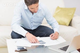 유토이미지 | Young man with bills calculator and laptop at home