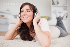 유토이미지 | Cheerful brunette woman using headphones while lying on a carpet