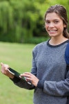 유토이미지 | Smiling student using her tablet pc while standing in a park