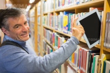 유토이미지 | Smiling man taking a tablet pc from shelves