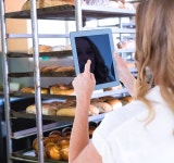 tablet pc against catering building with shelf of hot breads... Woman using tablet pc  against catering building with shelf of hot breads