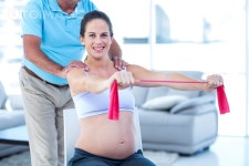 유토이미지 | Portrait of smiling pregnant woman stretching exercise band while therapist massaging