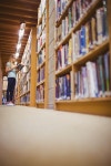 유토이미지 | Blonde student reading book next to bookshelf in library
