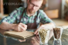 유토이미지 | Two glasses of coffee beans, raw and roasted on table in modern roastery with blurred form of barista taking notes... 
