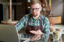 유토이미지 | Portrait of modern barista holding handful of fresh coffee beans using laptop while checking quality of roast in... 
