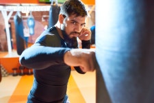 유토이미지 | Waist up portrait of fierce Middle-Eastern fighter hitting punching bag at boxing practice in martial arts club... 