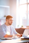 Young serious businessman concentrating on network while sitting by desk in front of laptop on sunny day | 유토이미지... 