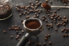 유토이미지 | Portafilter filled with ground coffee near spoon ang glass jar on dark wooden surface with coffee beans
