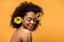 유토이미지 | Young sensual african american woman with artistic make-up and gerberas in hair isolated on orange background