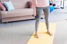 유토이미지 | cropped shot of woman standing on yoga mat with dumbbells at home