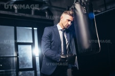 유토이미지 | handsome tired businessman in suit and boxing gloves leaning on punching bag in gym
