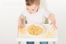 유토이미지 | high angle view of baby boy sitting in highchair and eating spaghetti by hands