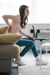 유토이미지 | side view of young woman sitting on sofa and suffering from back pain