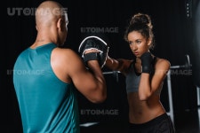 유토이미지 | rear view of muscular male trainer exercising with female boxer at gym