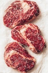 유토이미지 | top view of three pieces of raw meat steaks with salt on baking paper in kitchen