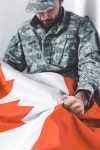 selective focus of depressed man in military uniform sitting in corner and holding canada national flag | 유토이미지... 