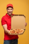 유토이미지 | happy delivery man in red uniform showing box with delicious pizza isolated on yellow