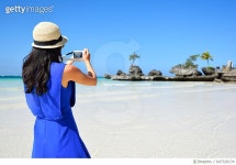 647320174 | 게티이미지코리아 | Young asian woman take picture using smartphone at beach Royalty-Free 이미지