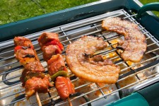 Man Turning and Roasting Chicken Filet, Pork Neck Steaks, Raw Fresh Sausages and Bacon Wrapped Dried Plums on Gas Grill BBQ Stock... 