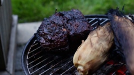 큰 쇠고기 양지머리와 껍질에 들어 있는 옥수수가 아래에 빛나는 석탄이 있는 작은 숯불 히바치 그릴에서 바비큐되고 있습니다. - HD... 