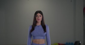 Sporty girl announcer addresses the camera with confidence from a well lit gym. Her athletic outfit and engaging demeanor set an... 