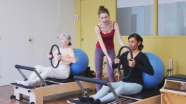 젊은 여성 강사와 그룹 운동을 하는 동안 필라테스 스튜디오에서 플렉스 링과 핏볼을 사용하여 운동하는 긍정적인 히스패닉 여성... 