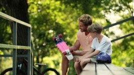 웃는 아버지는 여름에 공원 벤치에 앉아 페니 보드를 들고 어린 아들과 이야기를 나누고 있습니다. 무비클립, 동영상, 영상,HD 영상, HD... 