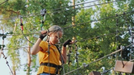 Premium stock video - A child climbs ropes high in the trees - having fun in a rope city in an amusement park