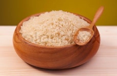 Raw rice in a bamboo bowl on a wooden surface over dark yellow background | Stock Photo | Colourbox