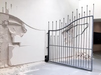 shilpa gupta's metal gate continuously swings back and forth breaking the wall behind it